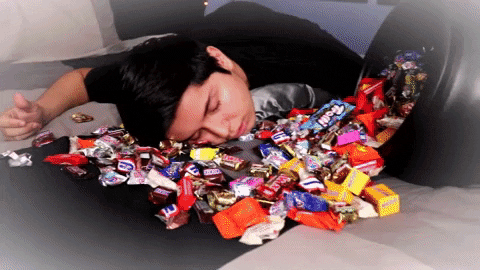 Gif of man lying in pile of Halloween candy, exhausted